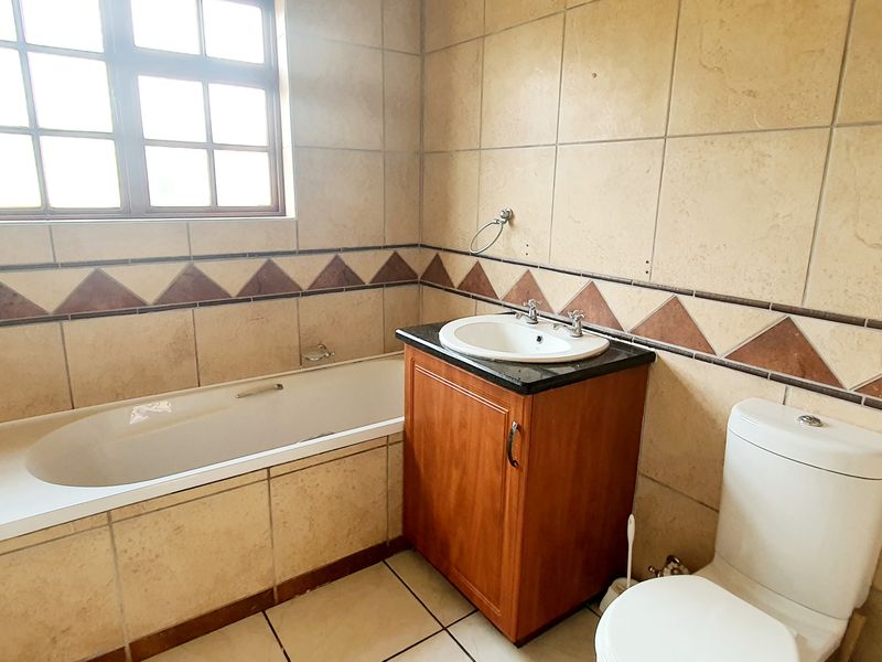 A functional bathroom featuring a built-in bathtub, vanity cabinet with granite countertop, and tiled finishes throughout.