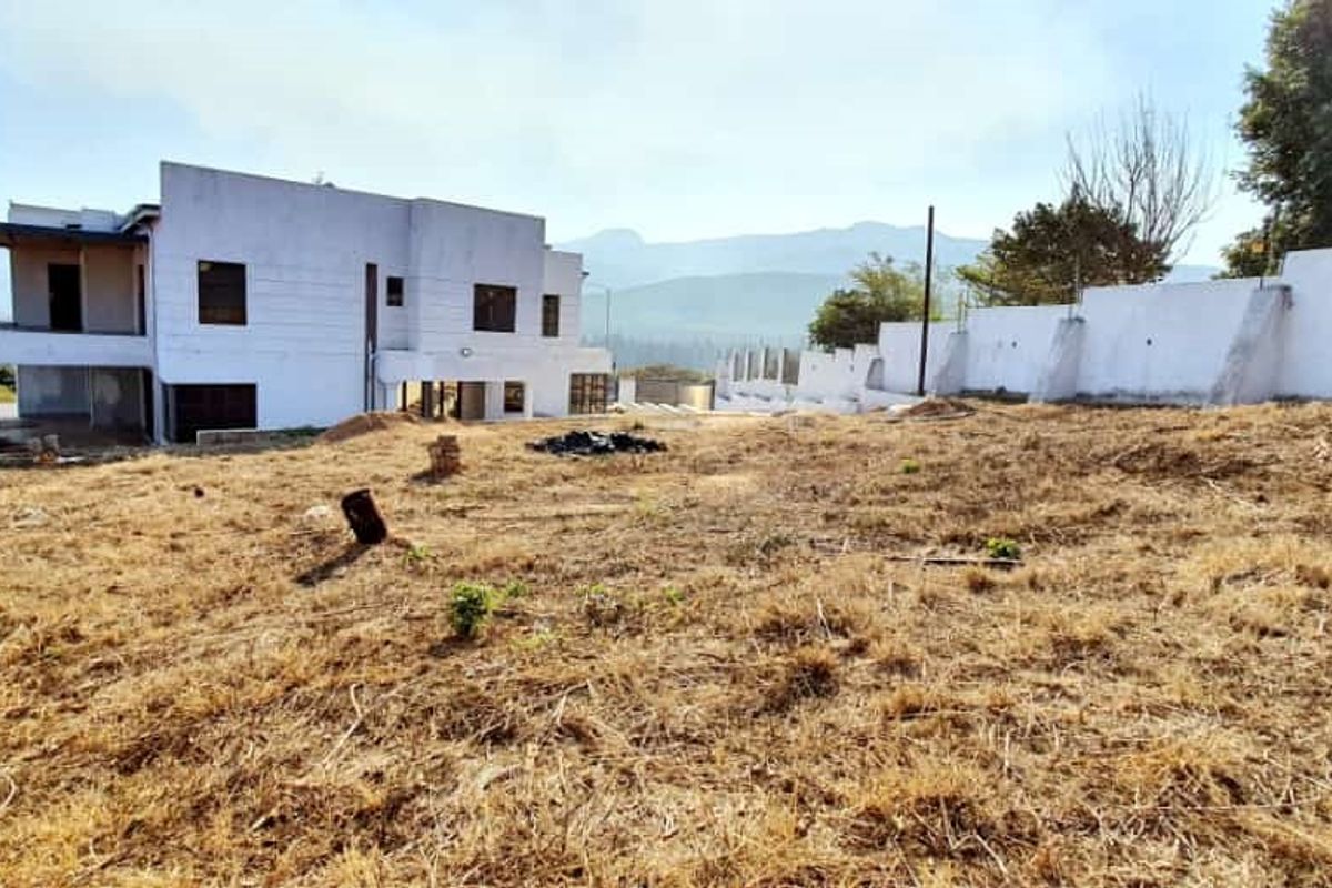 Rear view of the property showing a large unlandscaped yard, boundary wall, and the rear elevation of the house with a covered patio area.
