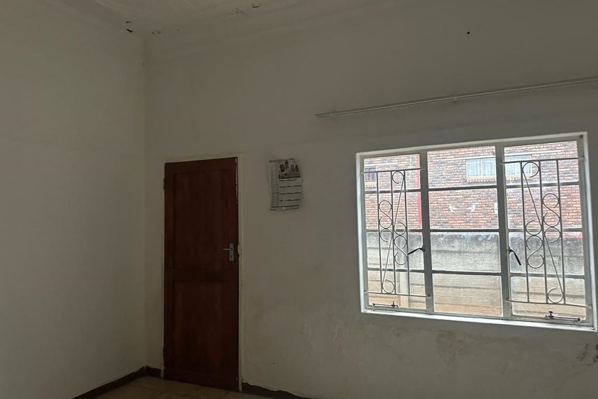 An empty bedroom featuring tiled flooring, a timber door, and a classic pressed metal ceiling, requiring cosmetic updates to the wall finishes.