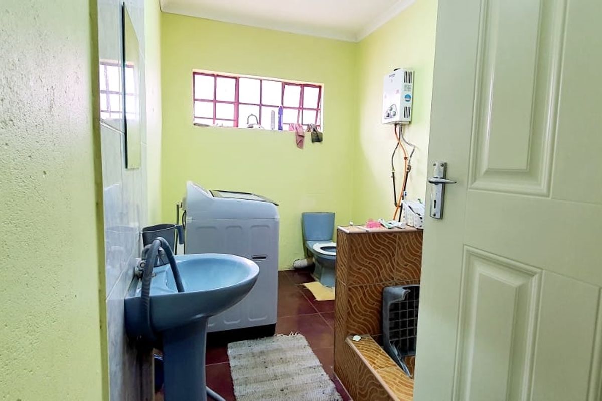 A functional bathroom featuring a pedestal basin, toilet, and tiled shower area with a wall-mounted gas geyser.