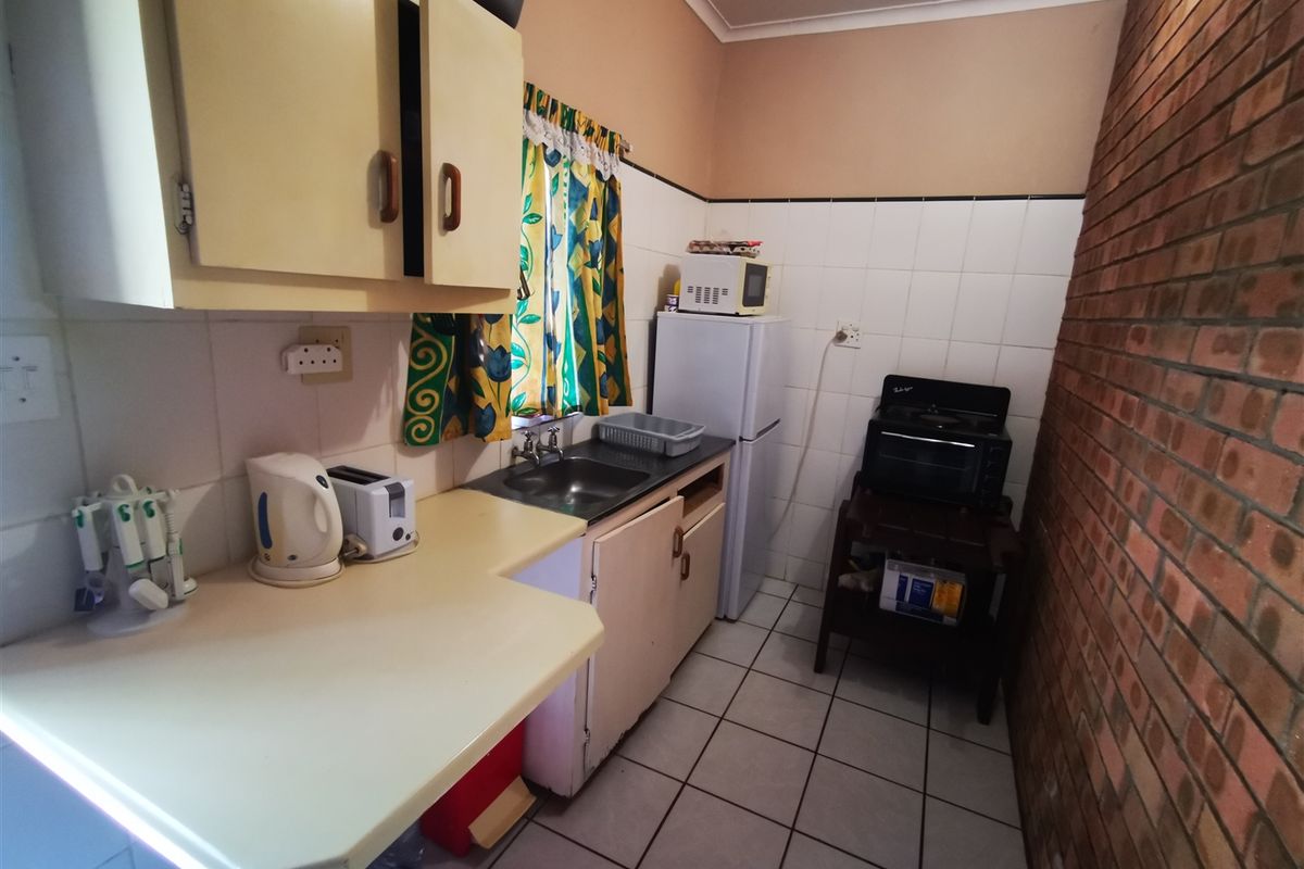 A compact kitchen featuring tiled flooring, exposed brick wall, built-in cabinetry, and a stainless steel sink, requiring cosmetic updates to modernize the space.