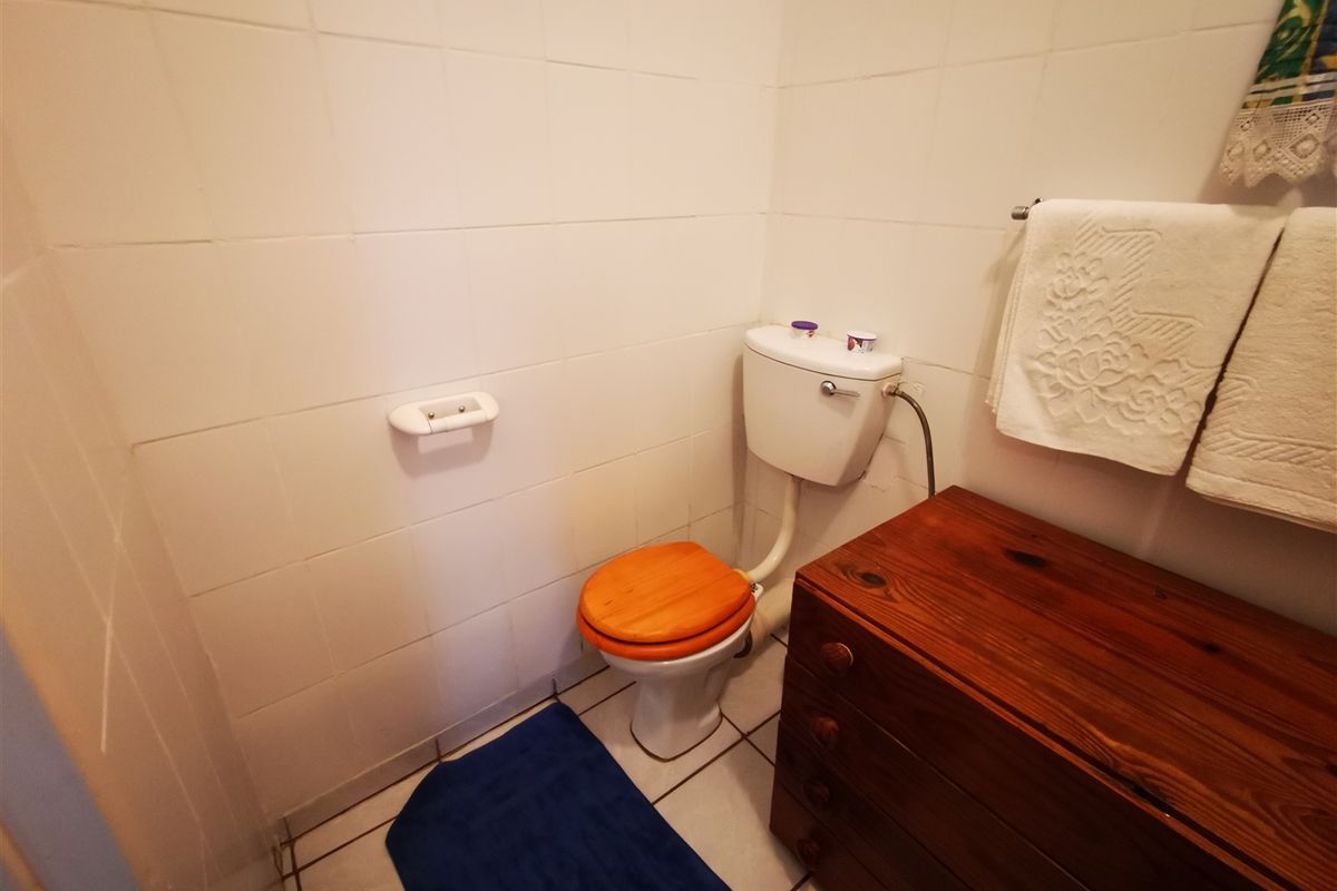 A compact bathroom featuring white wall tiles, ceramic floor tiling, and a standard toilet suite.