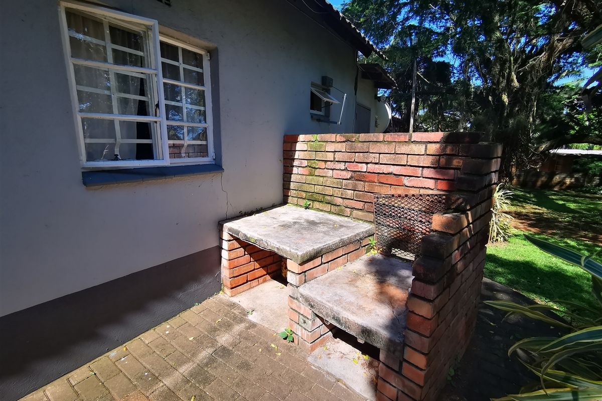 Rear exterior area featuring a built-in brick braai with concrete countertops, set on a paved patio adjacent to the main building structure.