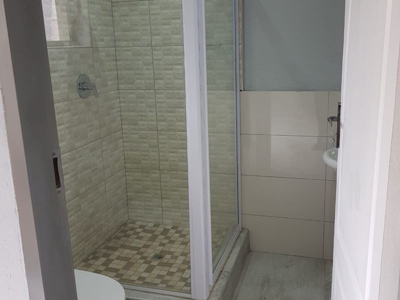 A clean, functional bathroom featuring a glass shower enclosure, tiled walls, and a standard toilet.