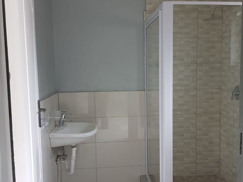 A functional bathroom featuring a shower enclosure, wall-mounted basin with mixer tap, and tiled finishes.