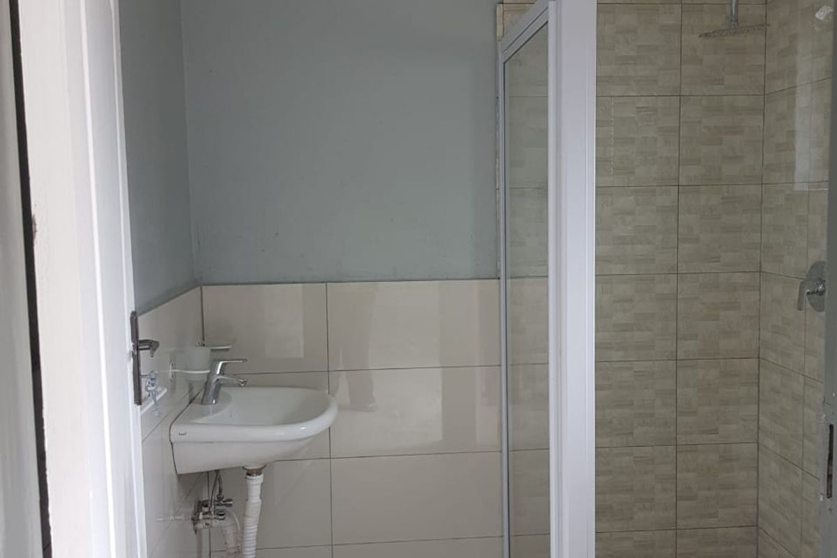 A functional bathroom featuring a shower enclosure, wall-mounted basin with mixer tap, and tiled finishes.