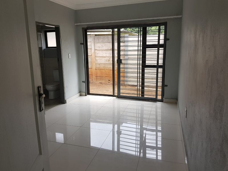 An empty bedroom featuring polished tiled flooring, a sliding glass door with a security gate, and direct access to an en-suite bathroom.