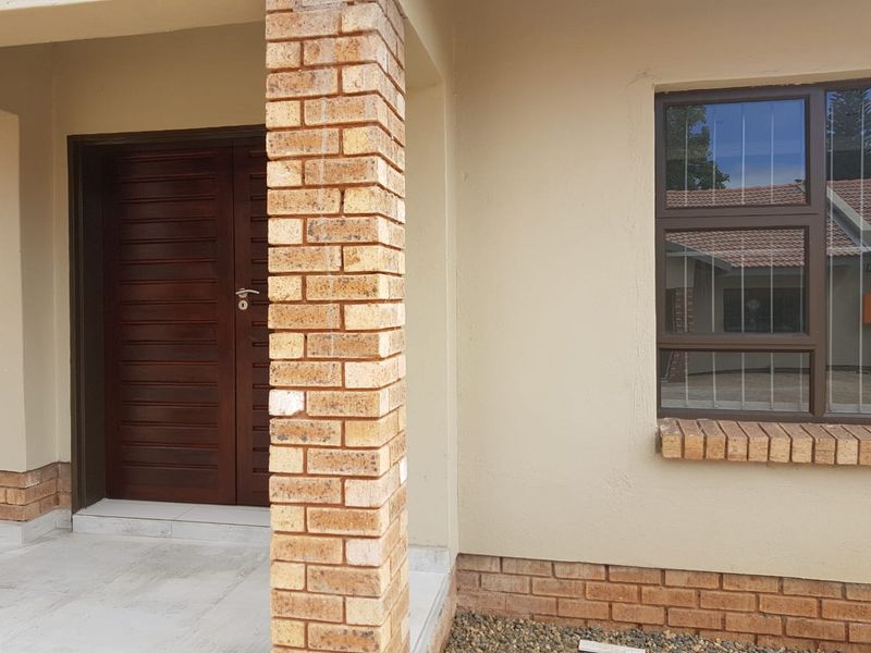 Front entrance featuring a solid timber door, brick pillar support, and aluminium window with security bars.