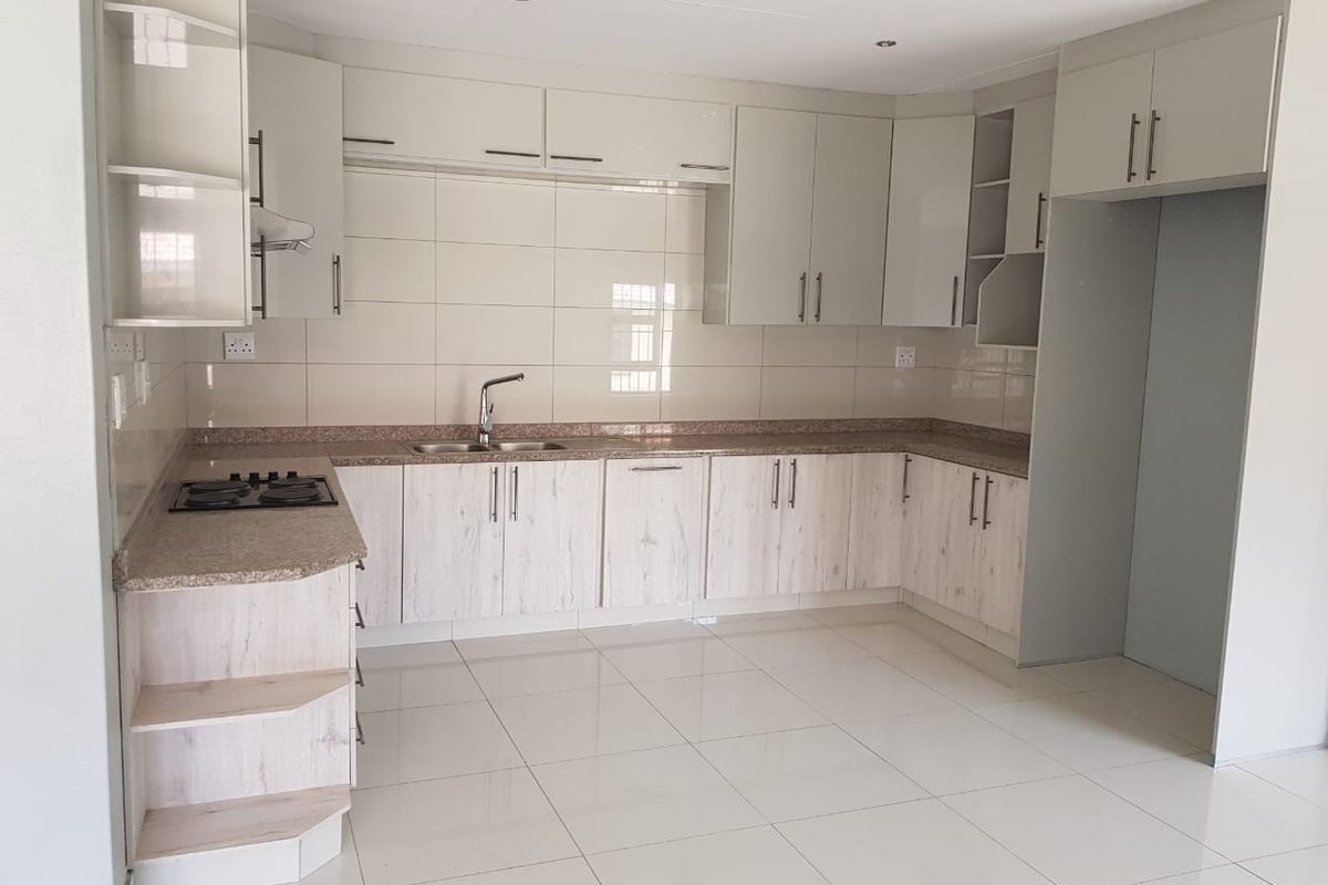 A clean, modern kitchen featuring light wood-grain cabinetry, granite countertops, a built-in gas hob, and neutral tiled flooring throughout.
