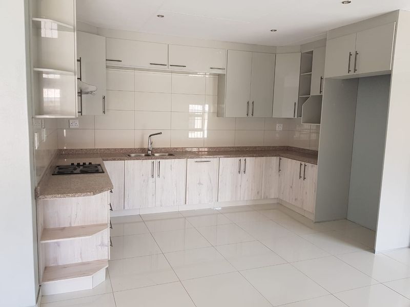 A clean, modern kitchen featuring light wood-grain cabinetry, granite countertops, a built-in gas hob, and neutral tiled flooring throughout.