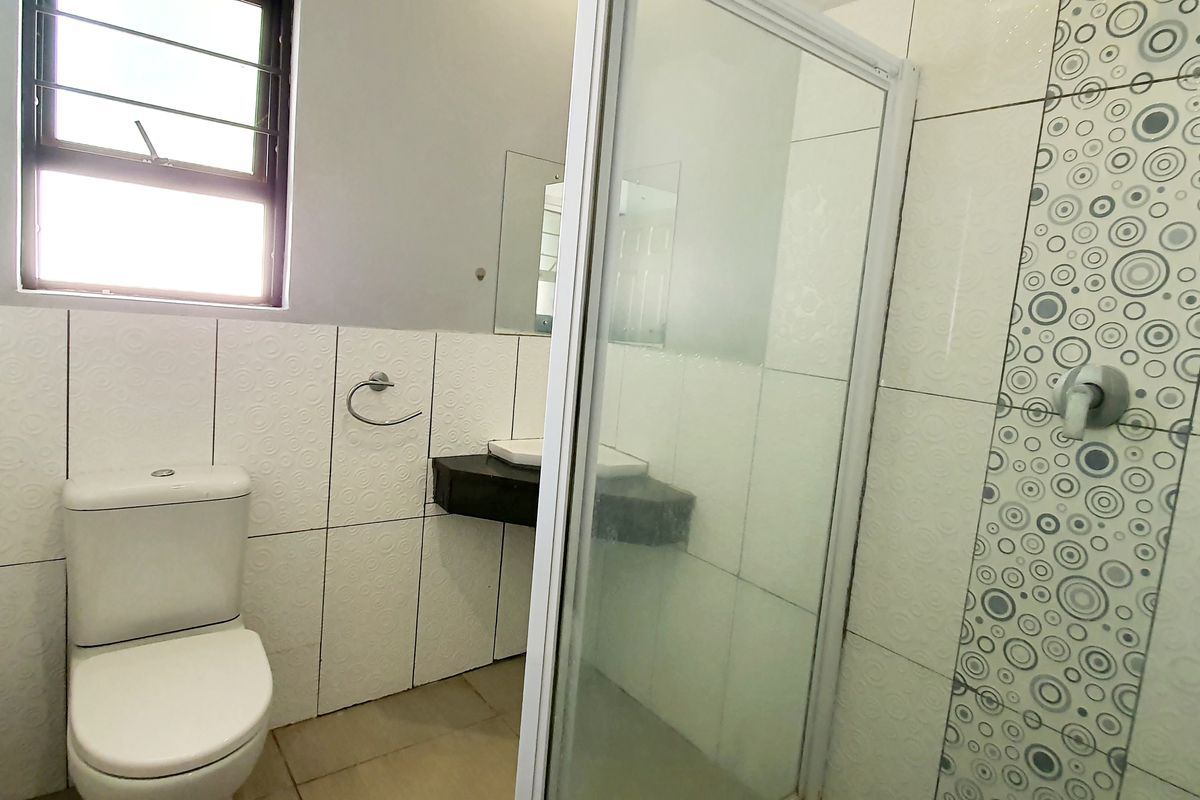 A functional bathroom featuring a shower enclosure, toilet, and wall-mounted basin with decorative tiled wall accents.