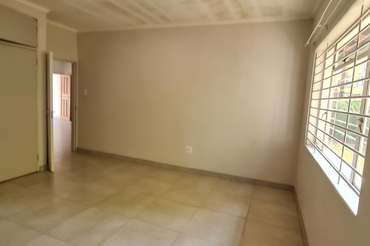 An empty bedroom featuring tiled flooring, built-in cupboards, and security bars on the window, offering a blank canvas for personalization.
