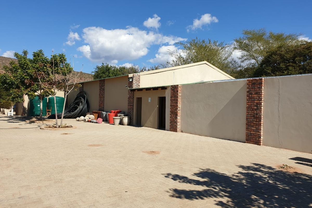 Rear exterior view of the retail property featuring a paved yard, plastered boundary walls with brick detailing, and external lighting.