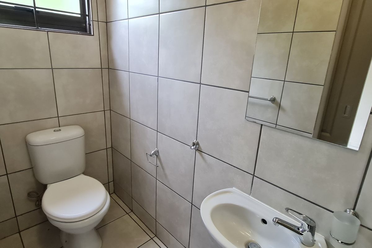 A compact guest bathroom featuring floor-to-ceiling neutral tiling, a wall-mounted mirror, a pedestal basin, and a standard toilet.