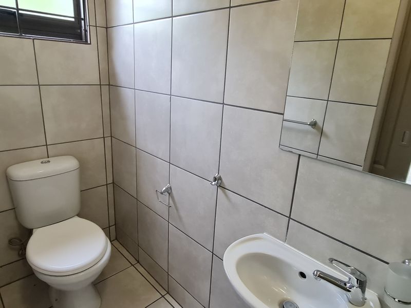 A compact guest bathroom featuring floor-to-ceiling neutral tiling, a wall-mounted mirror, a pedestal basin, and a standard toilet.