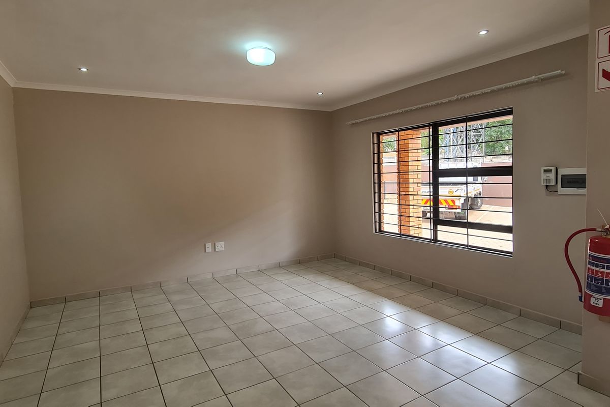 An empty living room featuring tiled flooring, security bars on the window, and a wall-mounted fire extinguisher.