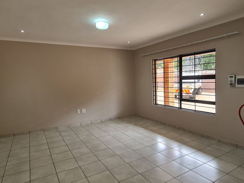 An empty living room featuring tiled flooring, security bars on the window, and a wall-mounted fire extinguisher.