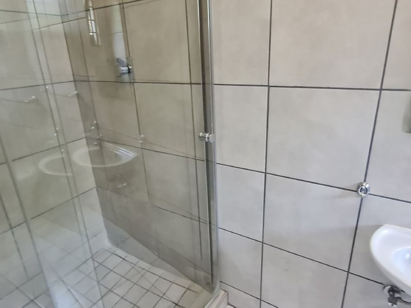A functional bathroom featuring a glass-enclosed shower, wall-mounted basin, and neutral wall tiling.
