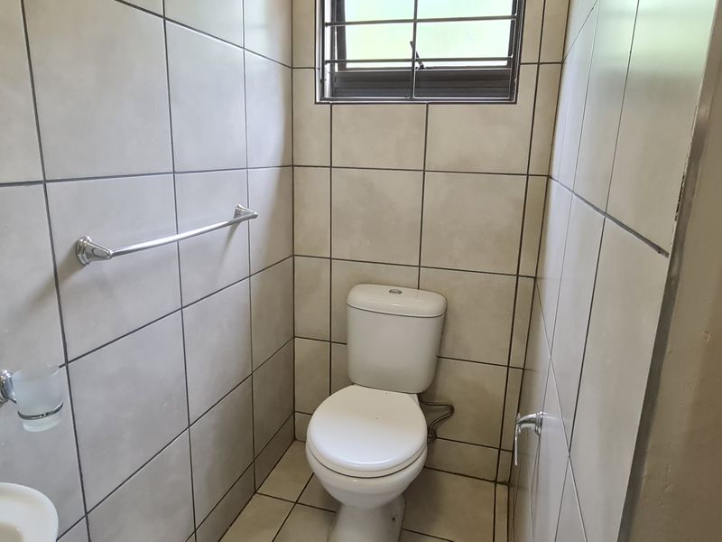 A compact guest bathroom featuring floor-to-ceiling wall tiles, a pedestal basin, and a standard toilet with a security-barred window.