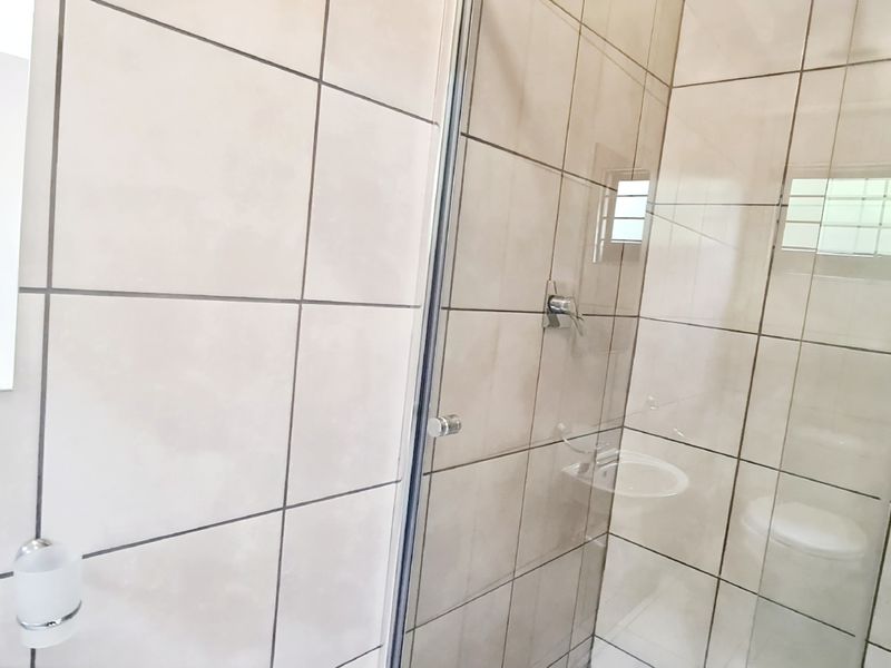 A functional bathroom featuring a glass-enclosed shower with neutral wall tiling and a wall-mounted mirror.