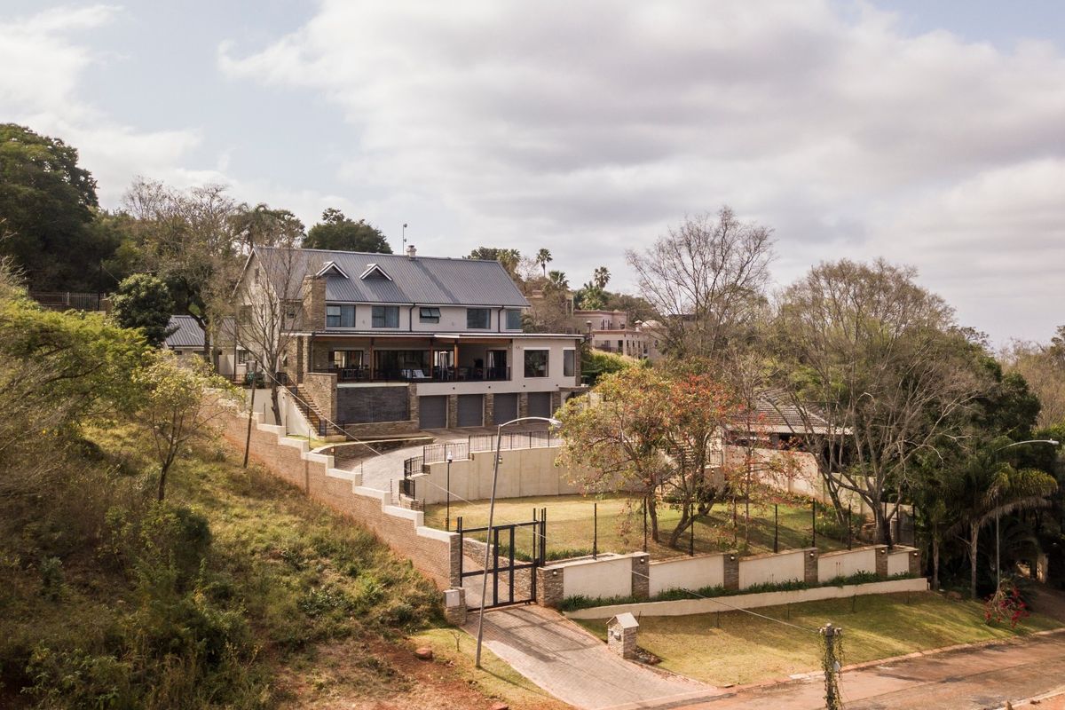 Aerial view of a multi-level residential property featuring a metal roof, stone accents, a spacious paved driveway, and extensive terraced retaining walls.