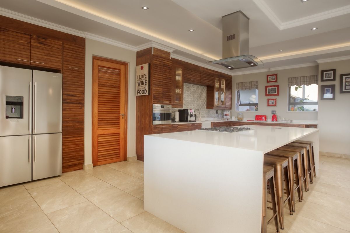 Modern kitchen featuring a large central island with stone countertops, high-end built-in appliances, warm wooden cabinetry, and recessed ceiling lighting.