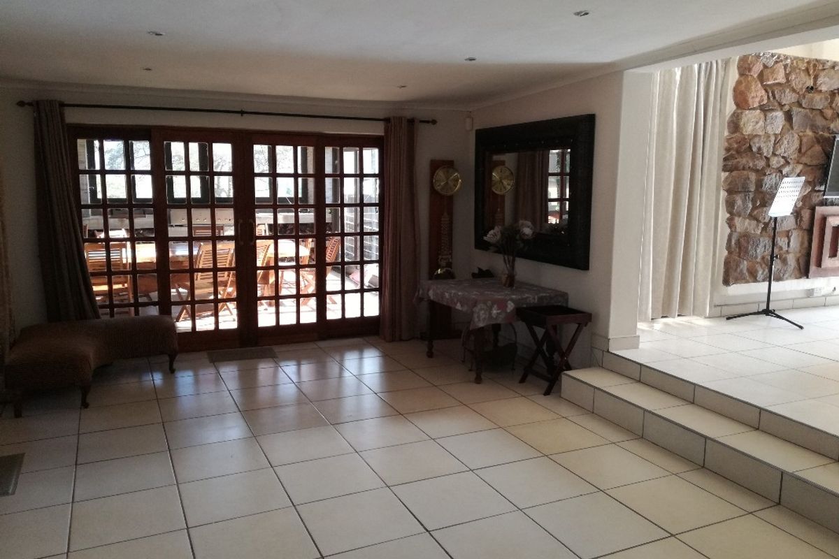 Spacious living area featuring tiled flooring, a stone feature wall, and large wooden framed glass doors leading to an outdoor patio.
