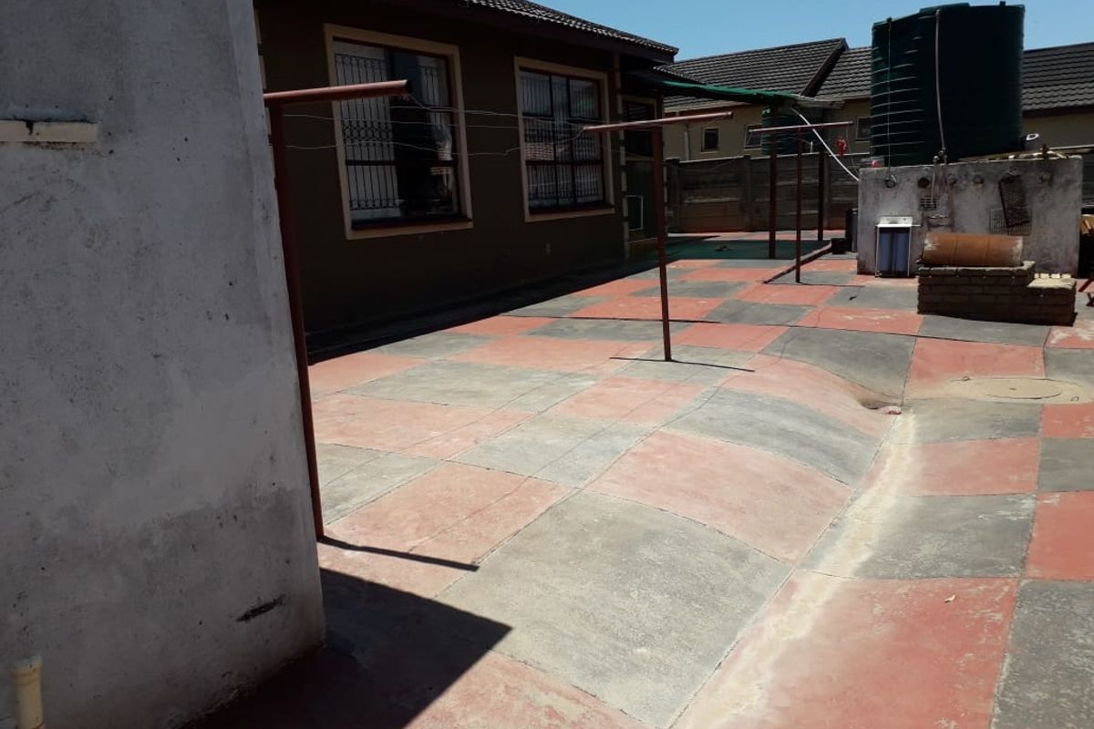 Rear exterior courtyard featuring a paved surface, water storage tank, and security-barred windows, offering a functional outdoor space with potential for landscaping improvements.