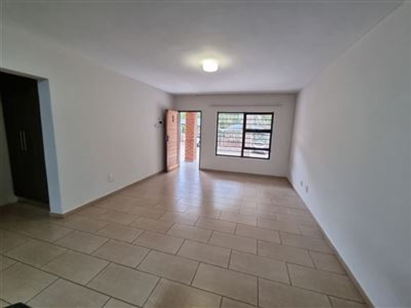 A spacious, empty living area featuring neutral tiled flooring, clean white walls, and natural light through an aluminium-framed window.