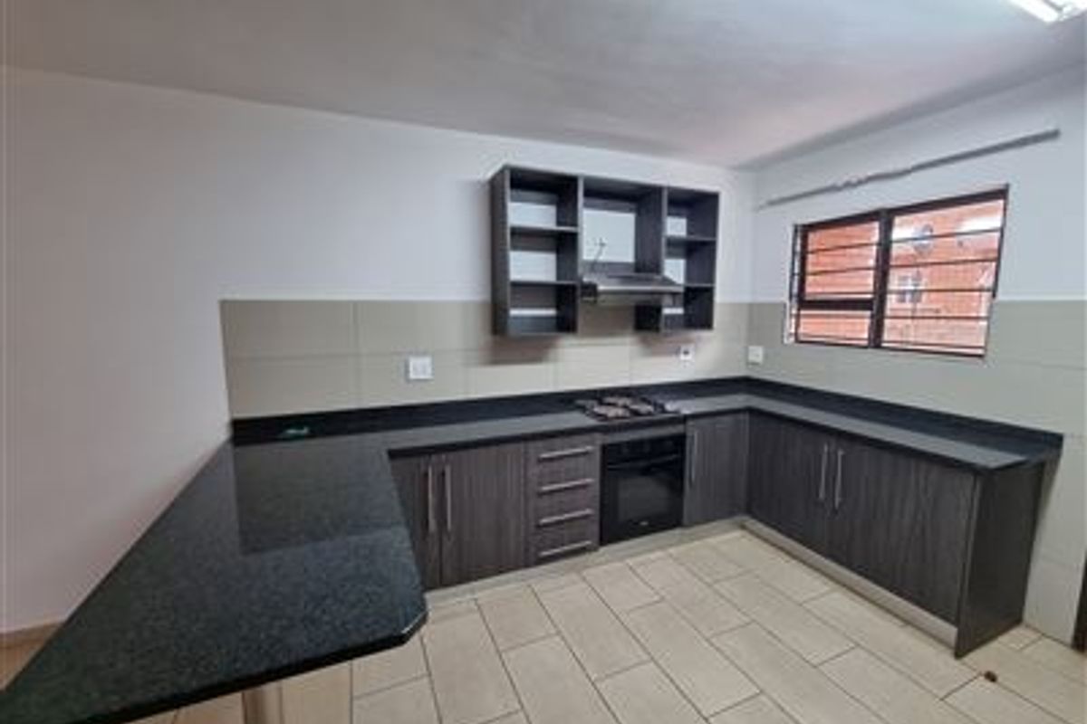 Modern kitchen featuring dark wood cabinetry, granite countertops, a breakfast bar, built-in oven, gas hob, and extractor fan with neutral tiled flooring.