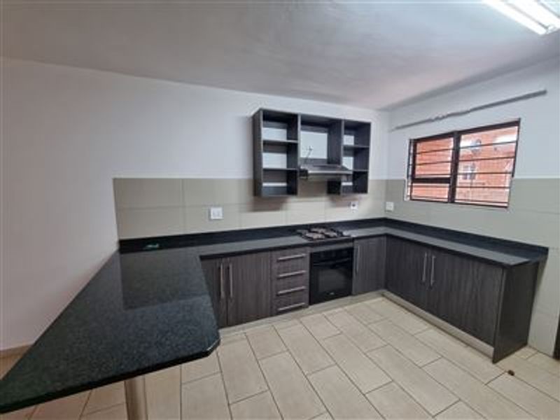 Modern kitchen featuring dark wood cabinetry, granite countertops, a breakfast bar, built-in oven, gas hob, and extractor fan with neutral tiled flooring.