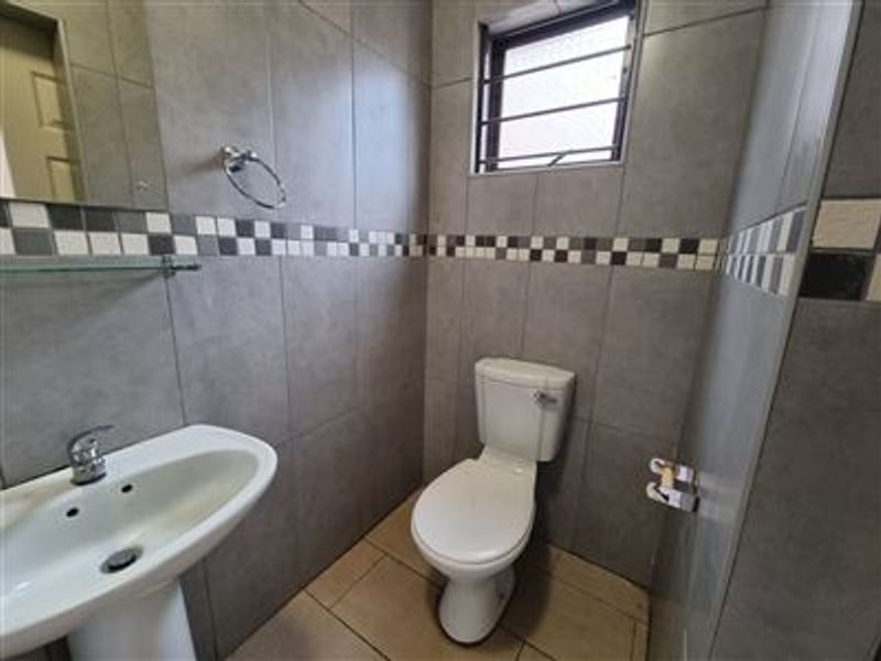 A compact guest bathroom featuring grey wall tiles with a decorative mosaic border, a pedestal basin, and a standard toilet.