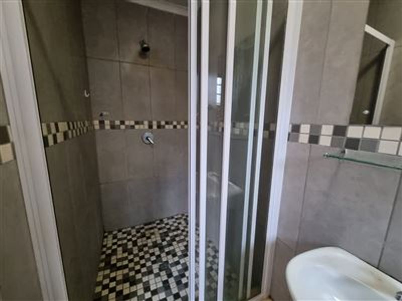 A functional bathroom featuring a shower enclosure with mosaic floor tiling, wall-mounted basin, and neutral wall tiles with a decorative mosaic border.