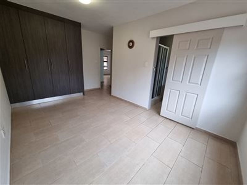 Spacious bedroom featuring neutral tiled flooring, dark wood-finish built-in cupboards, and a sliding door providing access to an en-suite bathroom.