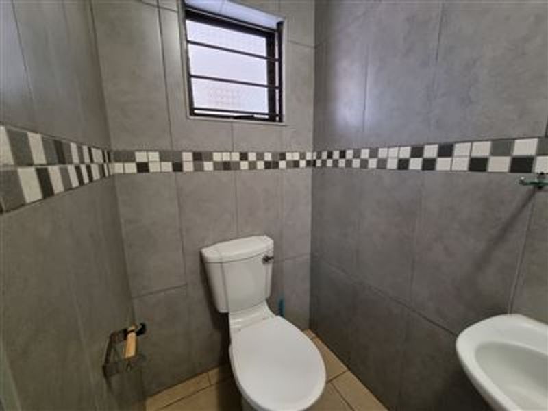 A compact, fully tiled bathroom featuring a standard toilet, washbasin, and a window with security bars.