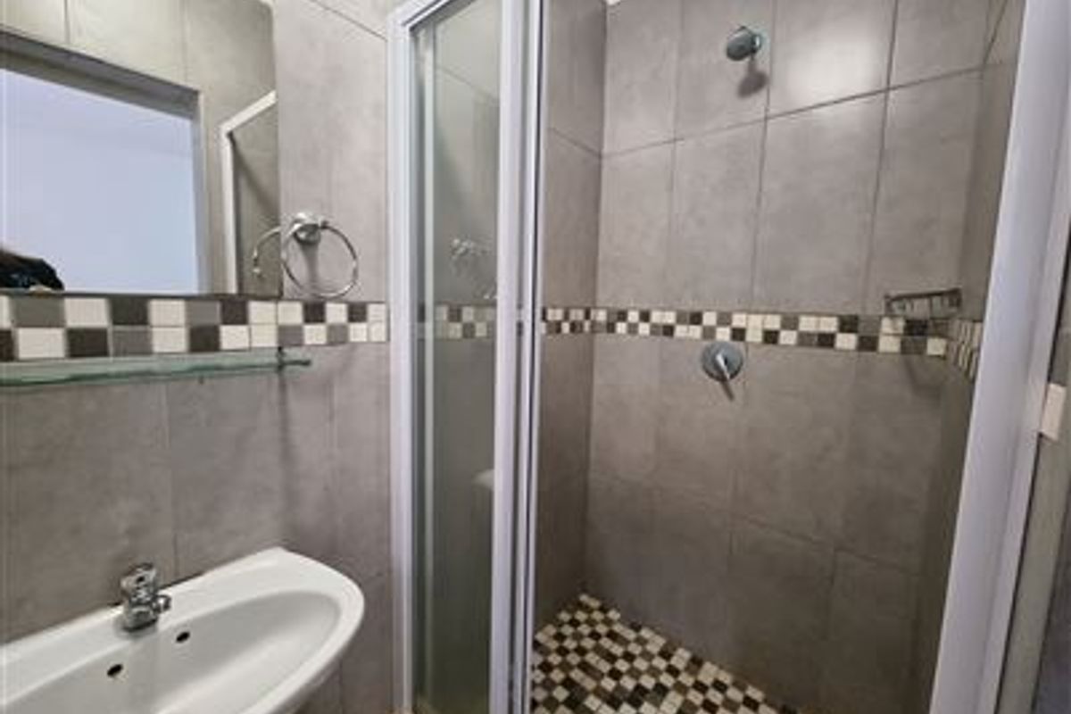 A compact bathroom featuring a tiled shower enclosure with mosaic accents, a wall-mounted basin, and neutral grey wall tiling.
