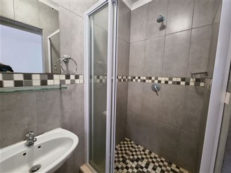 A compact bathroom featuring a tiled shower enclosure with mosaic accents, a wall-mounted basin, and neutral grey wall tiling.