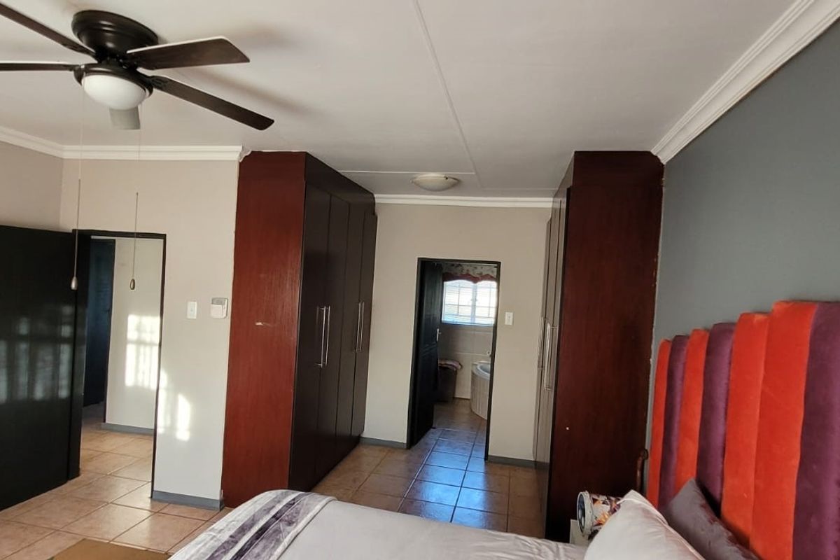 Spacious bedroom featuring built-in wooden cupboards, tiled flooring, and a ceiling fan, with direct access to an adjoining room.