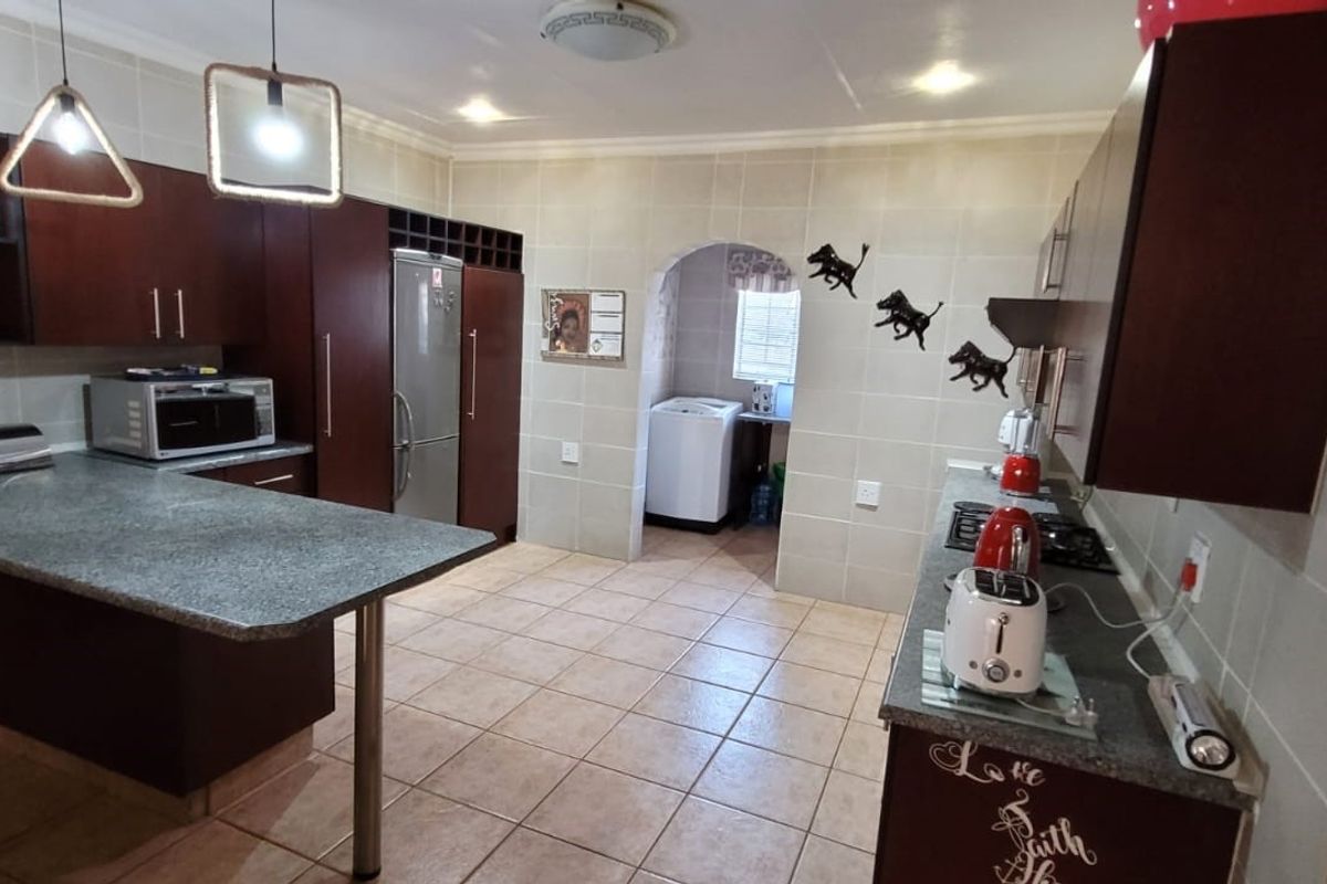 A functional kitchen featuring dark wood cabinetry, granite-look laminate countertops, tiled flooring, and an adjoining laundry area accessible through an arched doorway.
