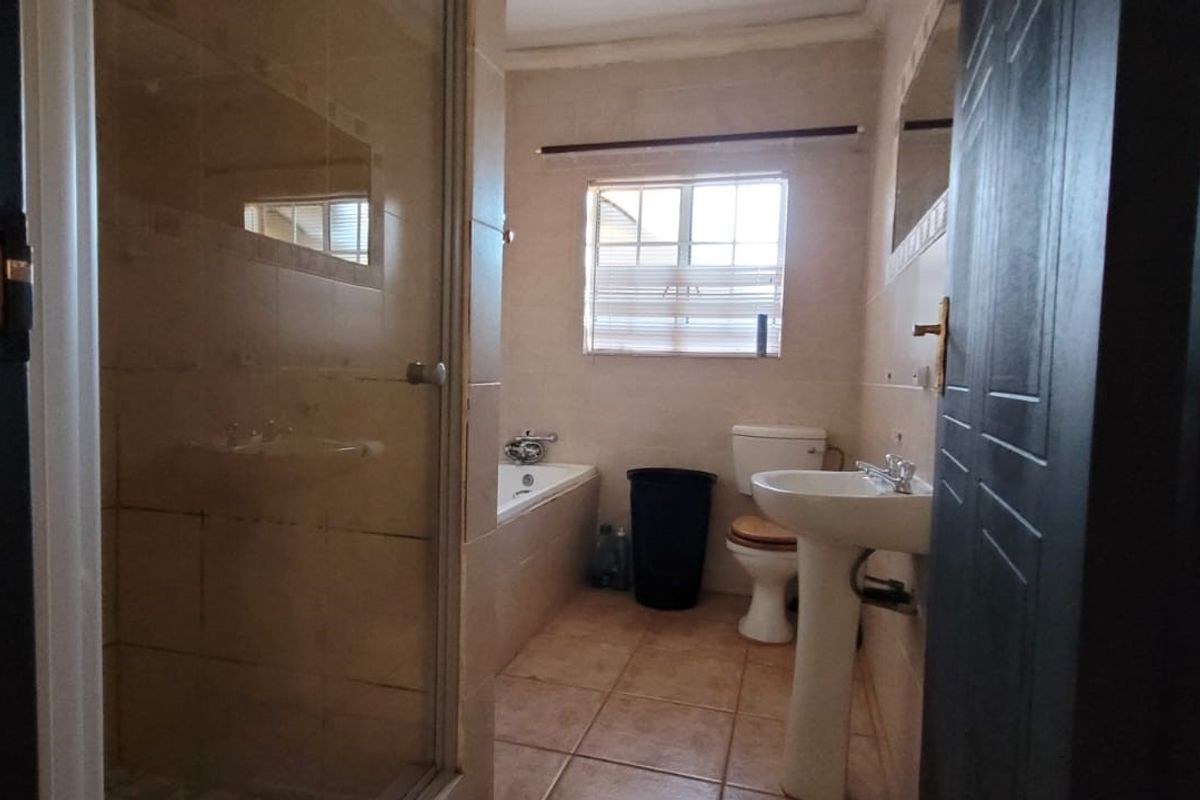 A functional bathroom featuring a shower enclosure, bathtub, pedestal basin, and toilet with neutral wall and floor tiling.