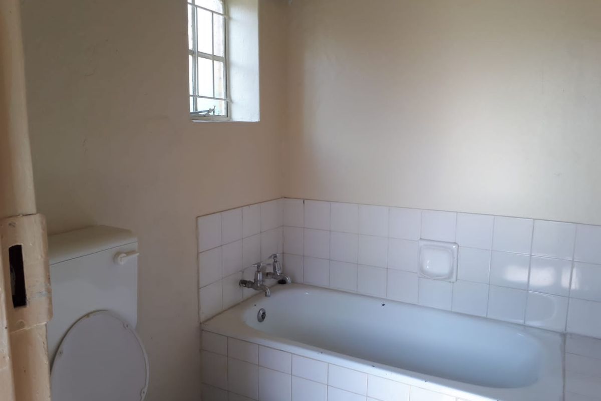 A functional bathroom featuring a built-in bathtub with tiled splashback and a standard toilet, requiring cosmetic updates to modernize the space.