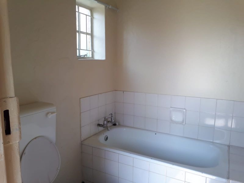 A functional bathroom featuring a built-in bathtub with tiled splashback and a standard toilet, requiring cosmetic updates to modernize the space.