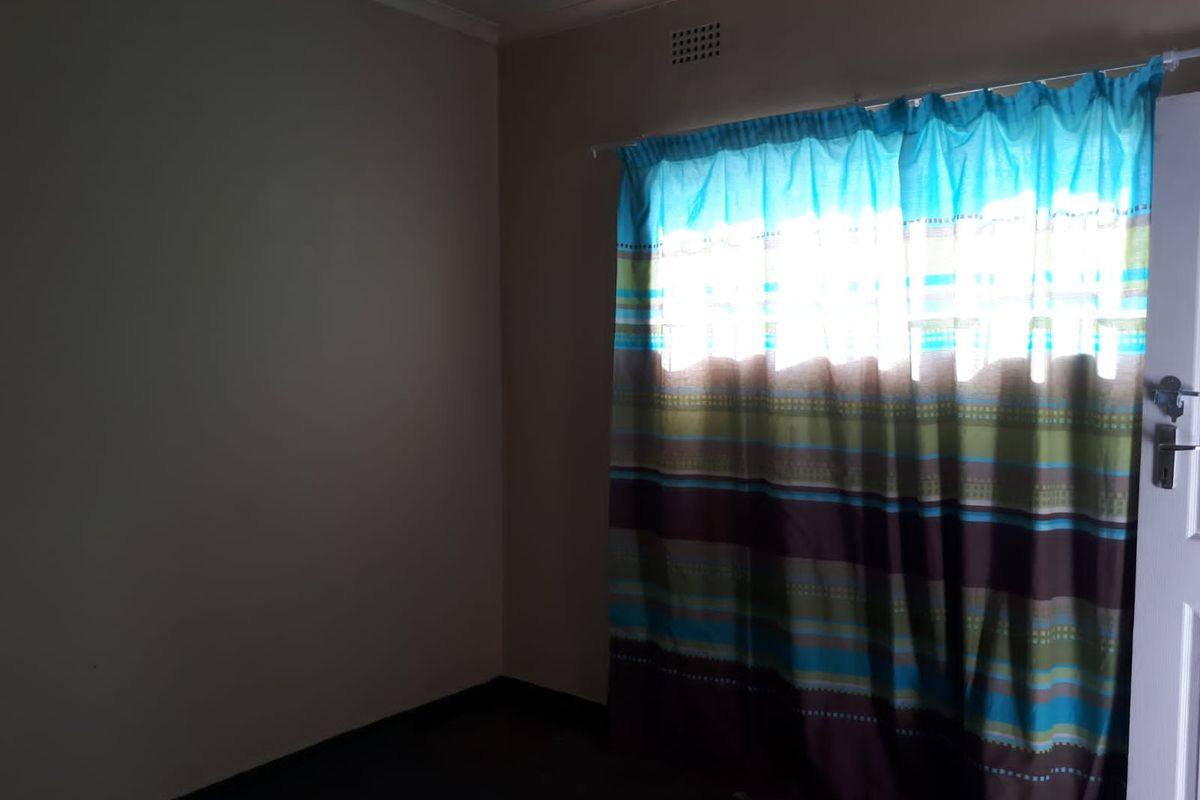 An empty bedroom featuring a window with a curtain rod and a ventilation grille, providing a blank canvas for interior design.