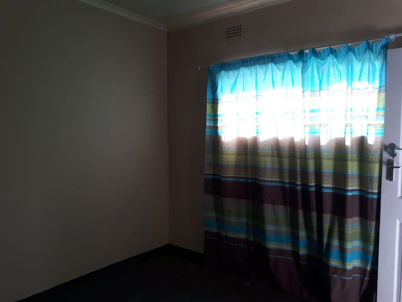An empty bedroom featuring a window with a curtain rod and a ventilation grille, providing a blank canvas for interior design.