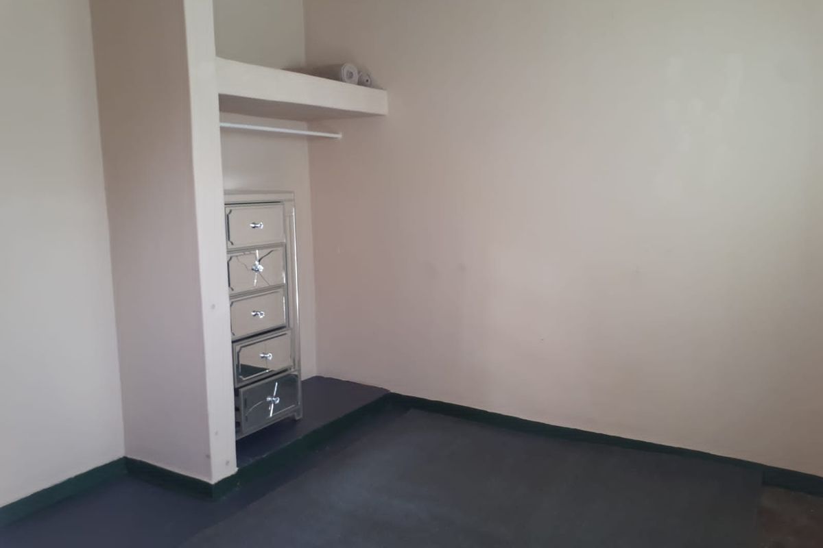A bedroom featuring a built-in closet with a shelf and hanging rail, finished with neutral wall paint and dark flooring.