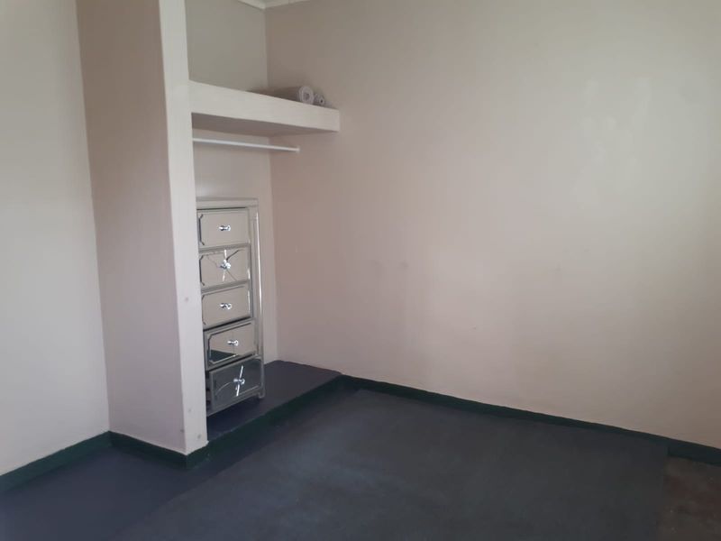 A bedroom featuring a built-in closet with a shelf and hanging rail, finished with neutral wall paint and dark flooring.