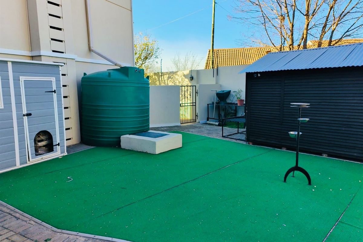 Rear outdoor area featuring a paved surface, water storage tank, and a secure metal storage shed against the boundary wall.