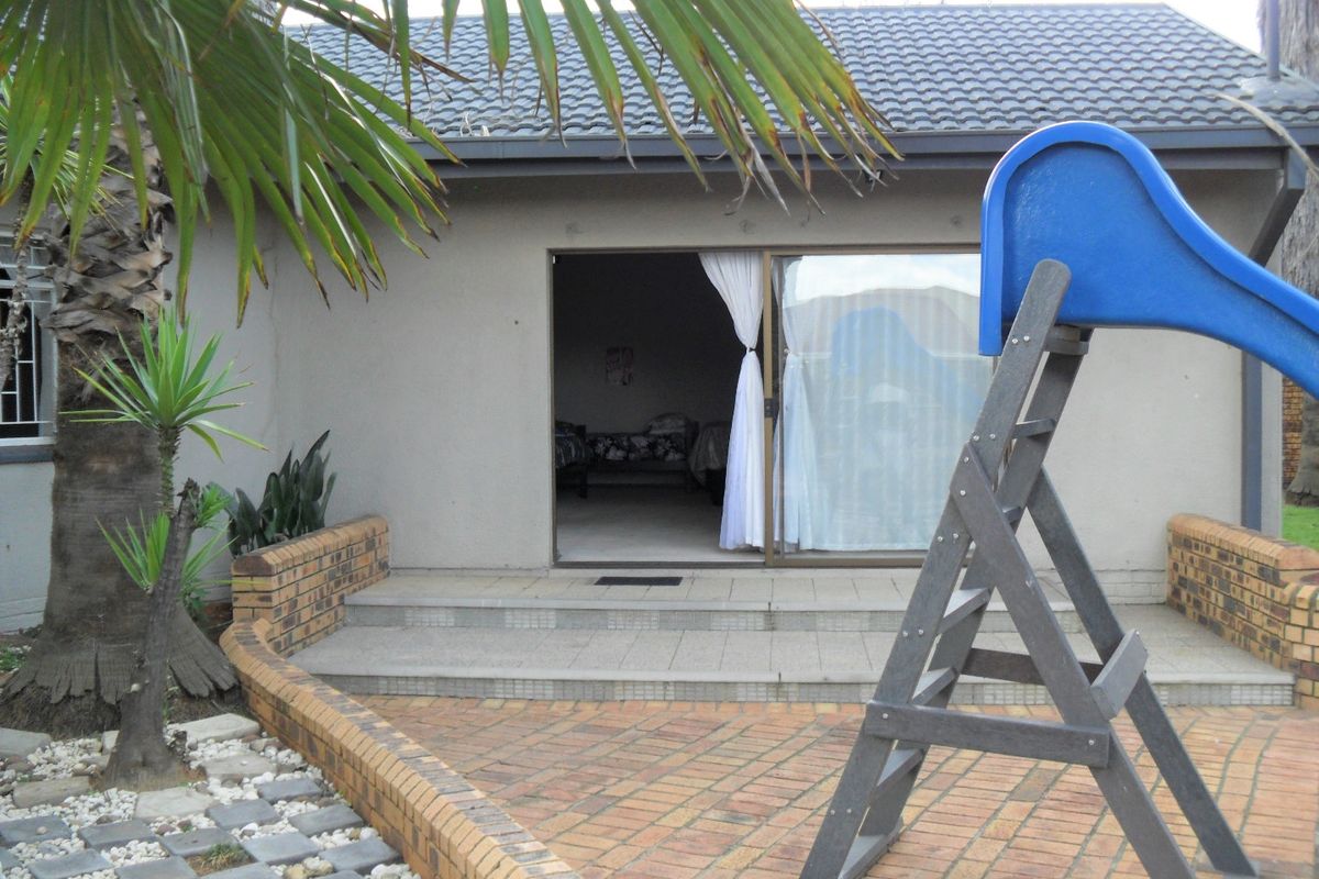Rear view of the property featuring a paved patio area, brick retaining walls, and a sliding glass door entrance.