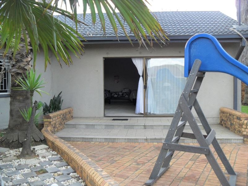 Rear view of the property featuring a paved patio area, brick retaining walls, and a sliding glass door entrance.