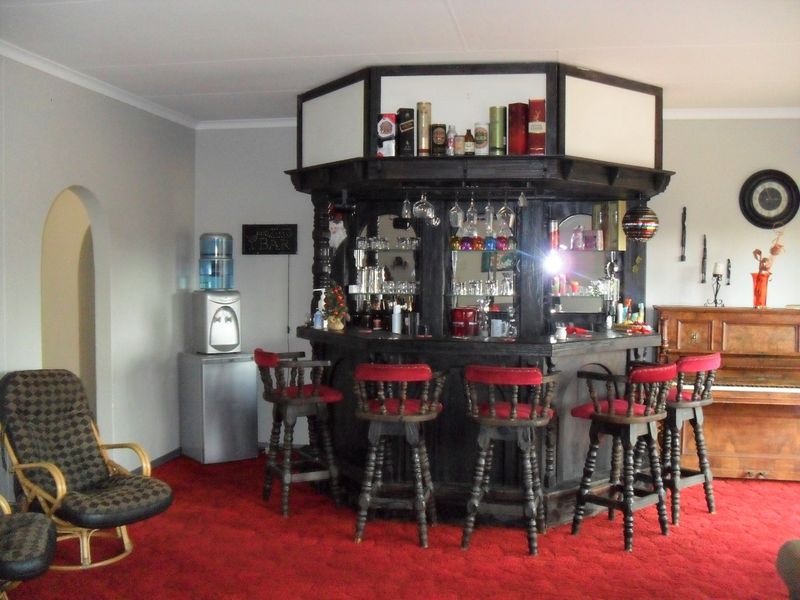 A dedicated home bar area featuring a built-in wooden bar counter with integrated shelving, mirrored back, and an adjacent arched doorway.